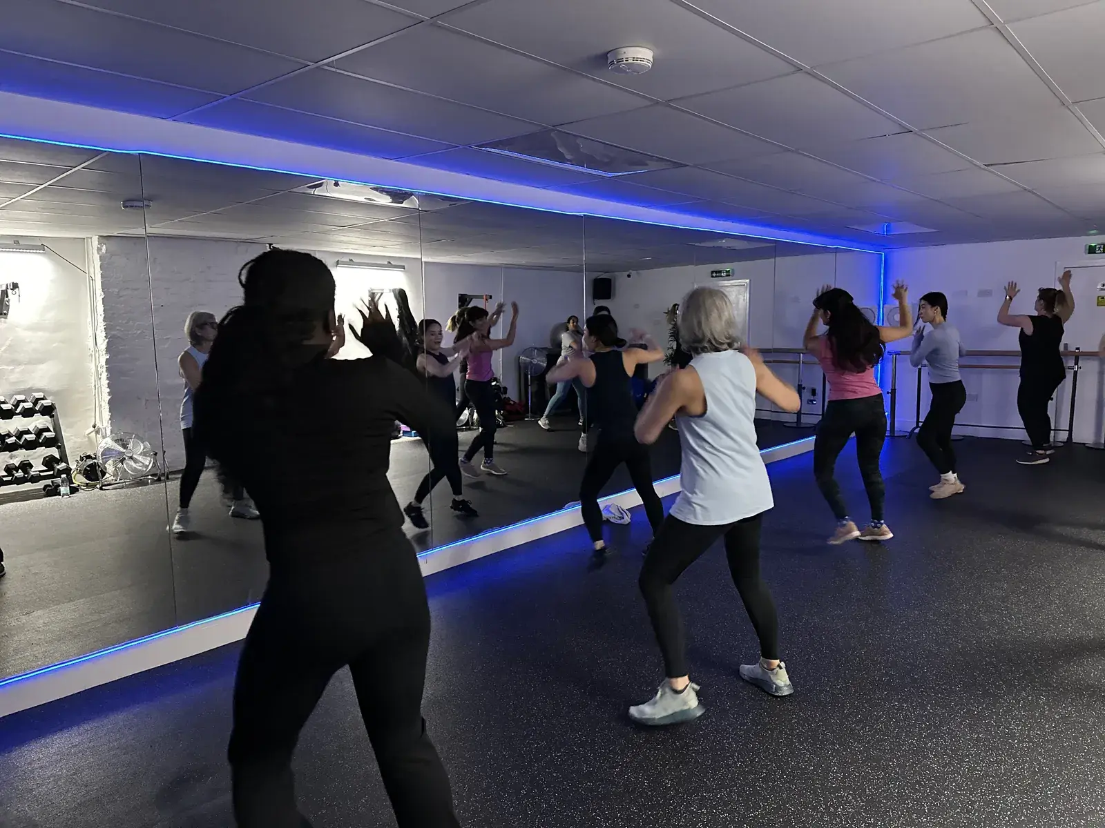 Zumba class dancing with arms raised under blue studio lighting